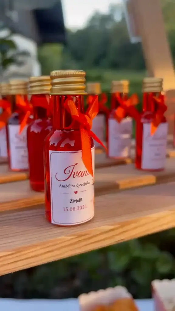 Mini bočice sa zlatnim čepom, narančastom vrpcom i personaliziranom etiketom s imenom gošće i datumom djevojačke večeri
