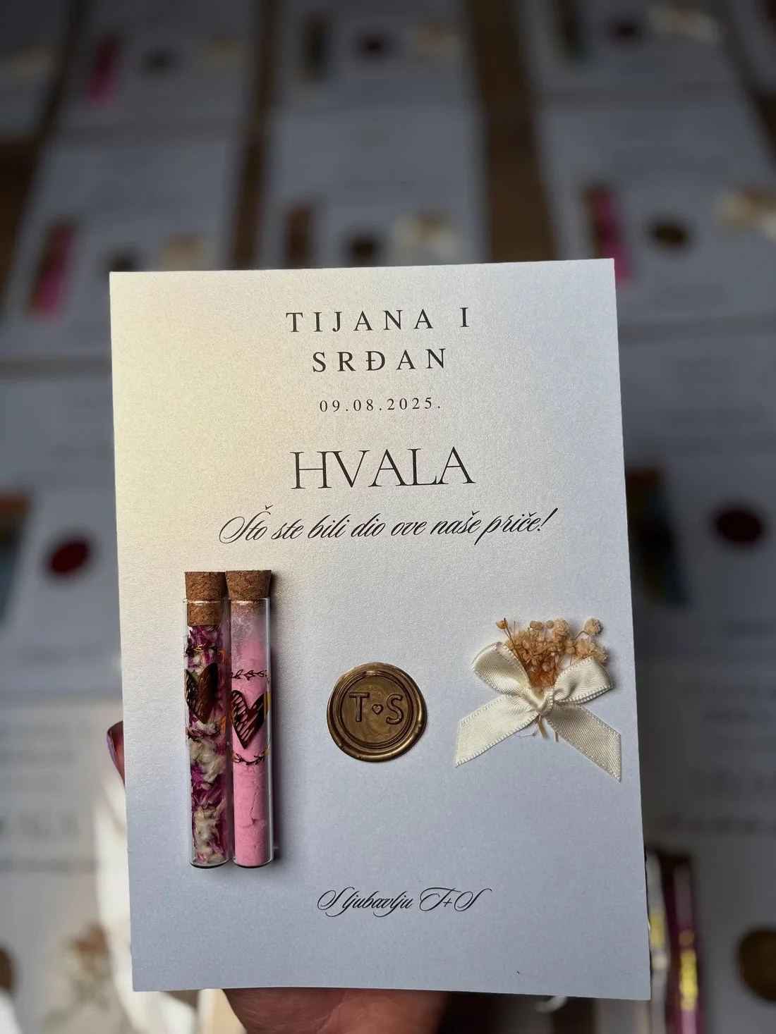 Kartica s imenima Tijana i Srđan, dvije epruvete s roza sušenim cvijećem, zlatni voštani pečat s monogramom i krem mašna